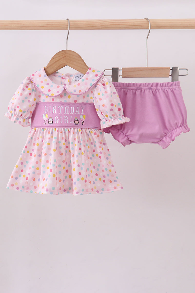 Baby girl's outfit with polka dot dress and pink bloomers on a hanger against a white background